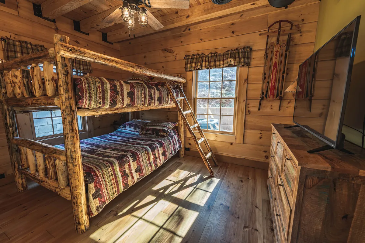 A family-friendly bedroom with a wooden bunk bed, a window letting in natural light, a sturdy dresser, ceiling fan, and playful decorative sleds. The atmosphere is inviting and versatile, well-suited for families or friends traveling together, and perfect for quiet reading or playful moments.