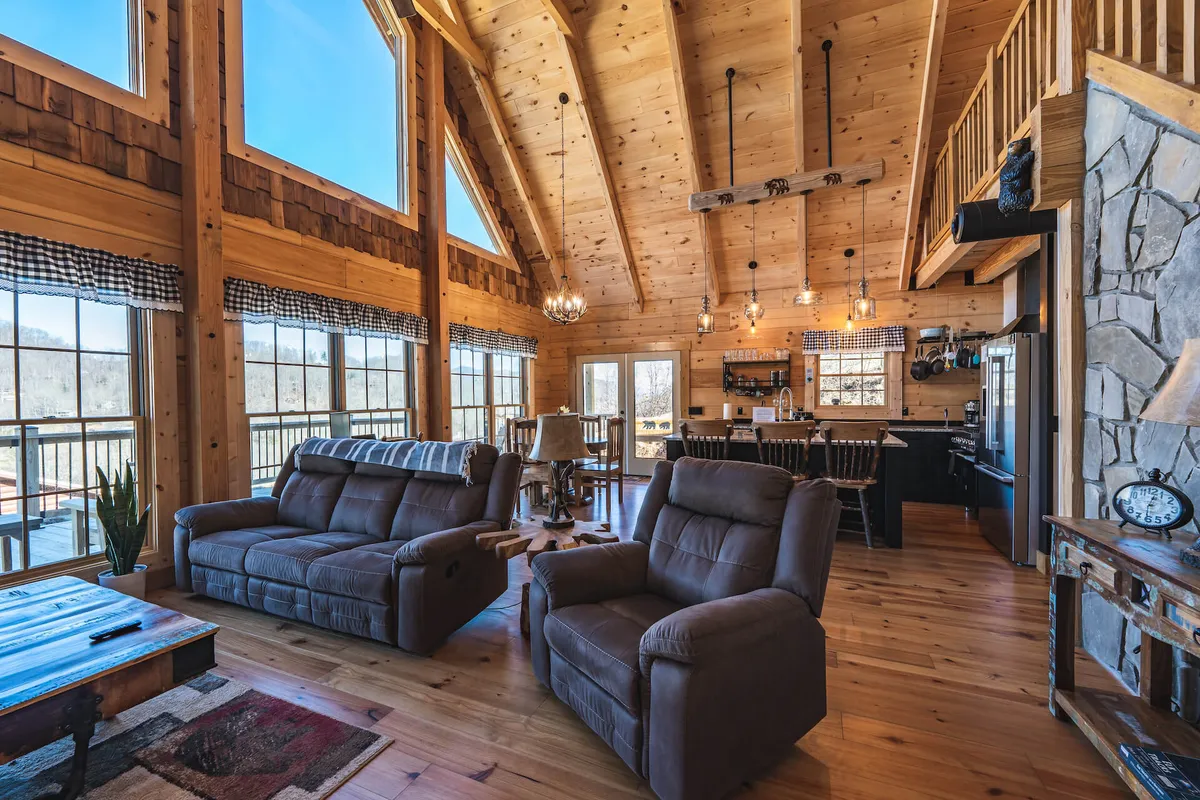 An inviting living and dining area with expansive windows looking out over a mountain landscape. Rustic décor, exposed wooden beams, and cozy seating create a warm, communal environment ideal for relaxation and connection.