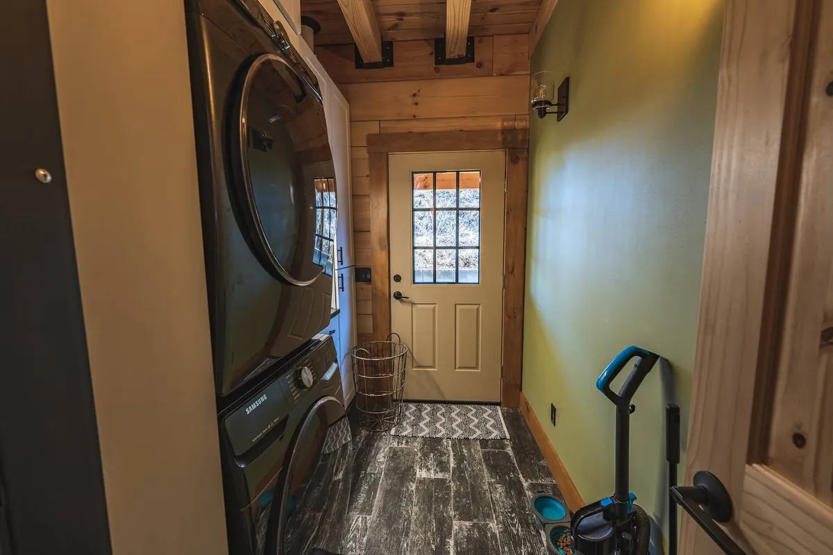 This image centers on a functional interior space with a washer and dryer, an entry door, and a decorative rug. The scene embodies a practical yet cozy environment that is perfect for managing outdoor gear, organizing belongings after an adventure, or greeting guests as they arrive.
