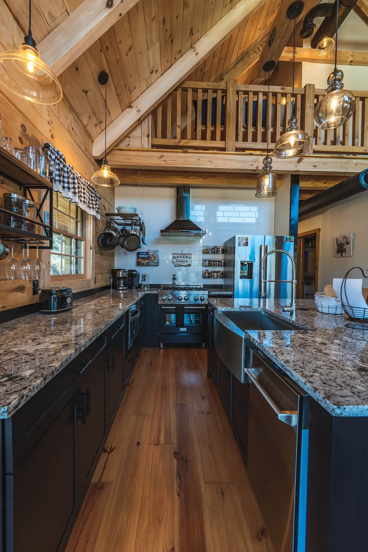 This image features a stylish kitchen with granite countertops, modern stainless steel appliances, exposed wooden beams, and warm hanging lights. The space is clearly designed for both cooking and socializing, with ample room for gathering and movement, and displays the cabin’s blend of rustic charm and contemporary conveniences.