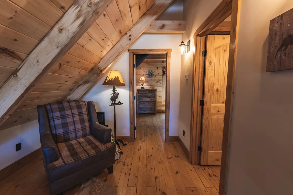 A welcoming living area featuring a plaid armchair, wooden lamp, wooden double doors, and decorative wall art. The scene is set for storytelling evenings or quiet reflection after a day outside.